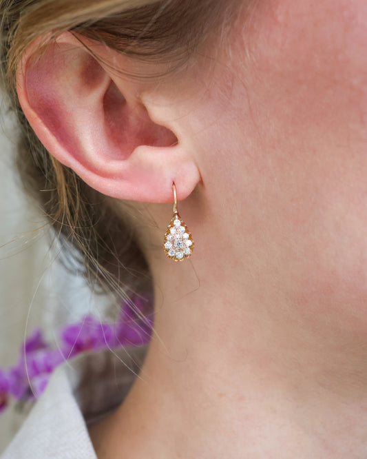 A teardrop cluster earring set with diamonds in yellow gold, modelled in an ear