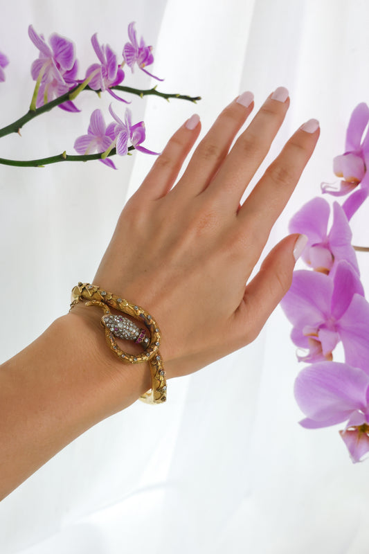 A yellow gold snake bangle bracelet set with diamonds and rubies, modelled on a wrist