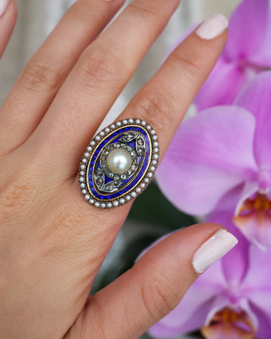 An oval antique ring set with pearls and diamonds, with a blue enamel background, in gold and silver, modelled on a hand
