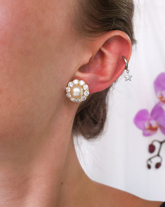 A round pearl and diamond cluster stud earring in yellow gold, modelled in an ear