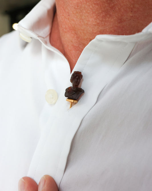 A carved chalcedony bust on a yellow gold stick pin, modelled in a white shirt buttonhole