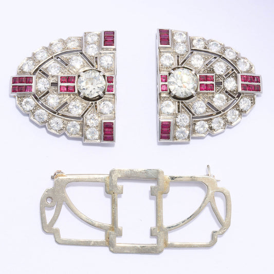 An Art Deco diamond and ruby double clip brooch, in an oval, geometric design, which can be worn as a single brooch or as a pair of dress clips on the neckline or collar of a dress. The design features two European old-cut diamonds, in four claw settings, alternating with groups of four calibré-cut rubies, in channel settings, with further, similarly set groups of six rubies, at the quarters; with an old-cut diamond, grain set, open work, plaque design, resembling arrow fletching, surrounding the centre pai