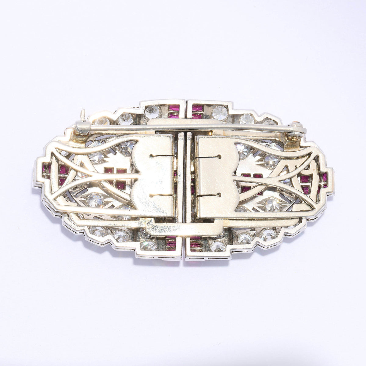 An Art Deco diamond and ruby double clip brooch, in an oval, geometric design, which can be worn as a single brooch or as a pair of dress clips on the neckline or collar of a dress. The design features two European old-cut diamonds, in four claw settings, alternating with groups of four calibré-cut rubies, in channel settings, with further, similarly set groups of six rubies, at the quarters; with an old-cut diamond, grain set, open work, plaque design, resembling arrow fletching, surrounding the centre pai
