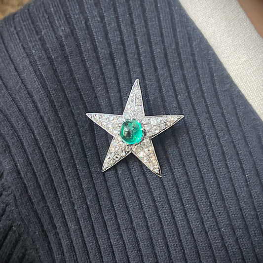 A star shaped brooch in silver and gold, with a cabochon emerald centre surrounded by old cut diamonds, modelled on a blue sweater