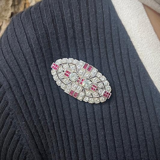 An Art Deco diamond and ruby double clip brooch, in an oval, geometric design, modelled on a blue sweater