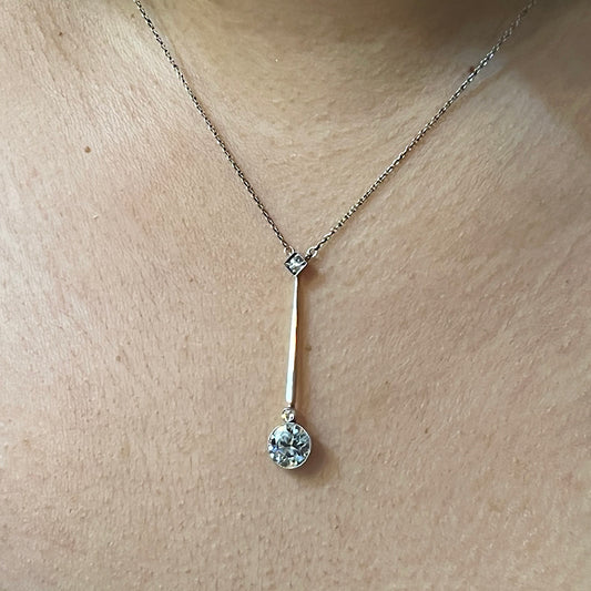 A round diamond bar drop pendant necklace with integrated chain, in platinum and gold, modelled