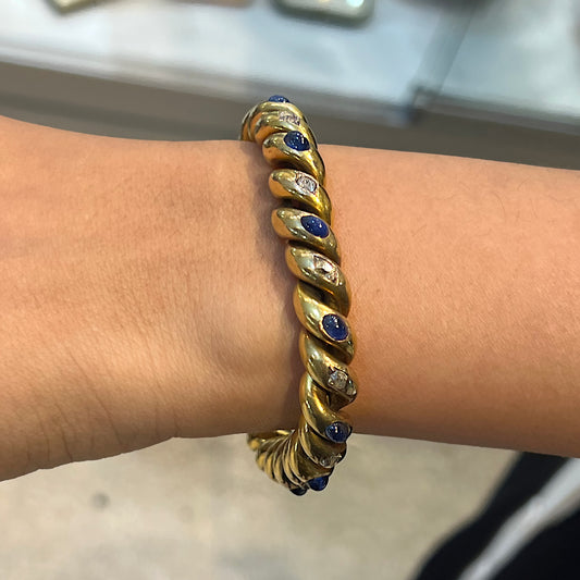 A yellow gold twisted bracelet set with cabochon sapphires and old cut diamonds, modelled on a wrist