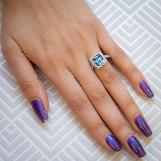 A cushion shaped aquamarine and round diamond cluster ring in platinum, with diamond set shoulders, modelled on a hand
