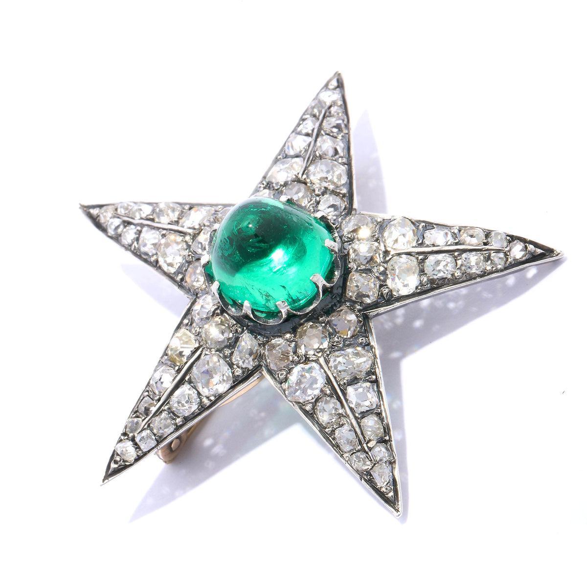 A star shaped brooch in silver and gold, with a cabochon emerald centre surrounded by old cut diamonds