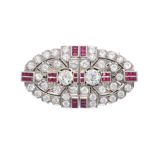 An Art Deco diamond and ruby double clip brooch, in an oval, geometric design, which can be worn as a single brooch or as a pair of dress clips on the neckline or collar of a dress. The design features two European old-cut diamonds, in four claw settings, alternating with groups of four calibré-cut rubies, in channel settings, with further, similarly set groups of six rubies, at the quarters; with an old-cut diamond, grain set, open work, plaque design, resembling arrow fletching, surrounding the centre pai