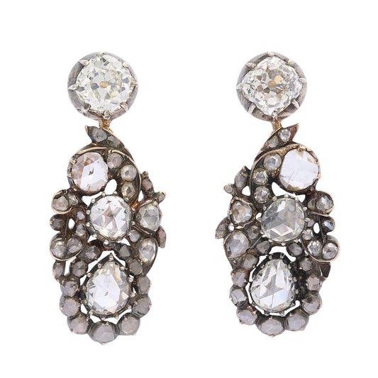 A pair of diamond, silver and gold cluster drop earrings, with stud tops, with old-cut diamonds, in cut down settings, with fancy cluster drops, set with three larger rose-cut diamond, the bottom diamonds are&nbsp; pear shaped, with surrounding, smaller rose-cut diamonds, in a scrolling foliate design, in cut down settings, mounted in silver-upon-gold, circa 1880.
