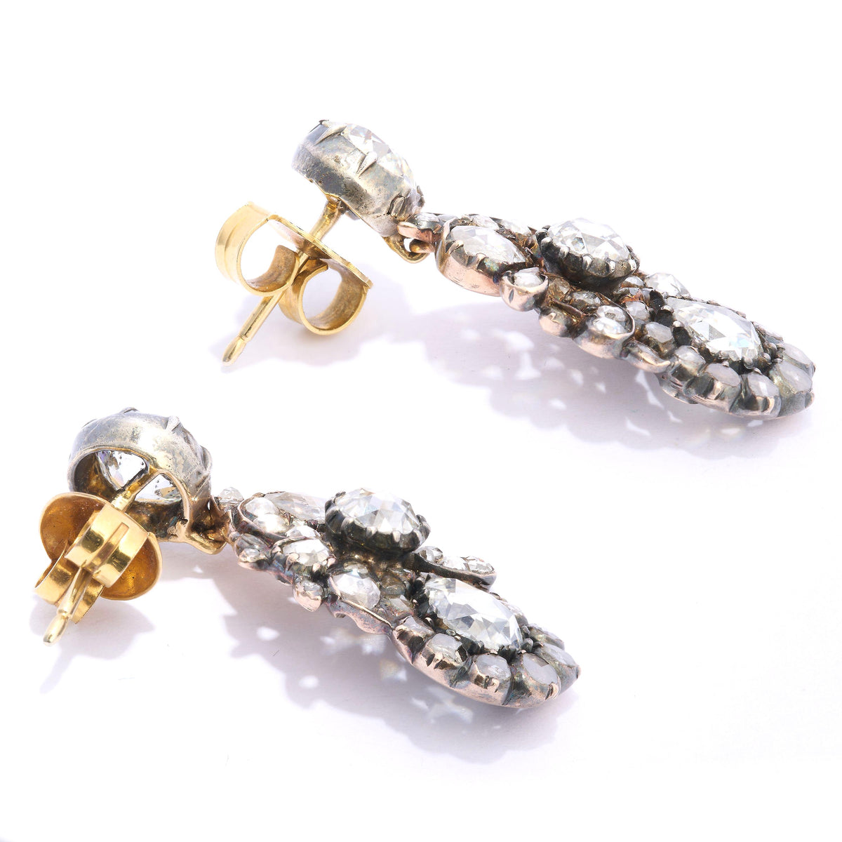 A pair of diamond, silver and gold cluster drop earrings, with stud tops, with old-cut diamonds, in cut down settings, with fancy cluster drops, set with three larger rose-cut diamond, the bottom diamonds are&nbsp; pear shaped, with surrounding, smaller rose-cut diamonds, in a scrolling foliate design, in cut down settings, mounted in silver-upon-gold, circa 1880.