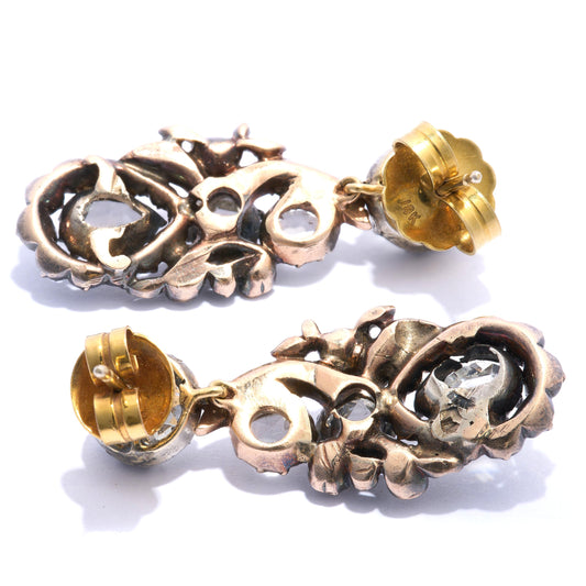 A pair of diamond, silver and gold cluster drop earrings, with stud tops, with old-cut diamonds, in cut down settings, with fancy cluster drops, set with three larger rose-cut diamond, the bottom diamonds are&nbsp; pear shaped, with surrounding, smaller rose-cut diamonds, in a scrolling foliate design, in cut down settings, mounted in silver-upon-gold, circa 1880.