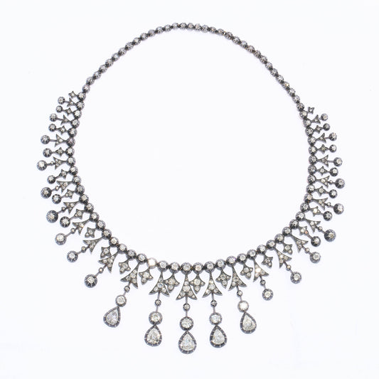 An antique French diamond fringe drop tiara necklace, featuring a graduating fringe of alternating, old mine-cut diamond, grain set, trefoils and arrowheads, with round, old mine-cut diamonds below, in cut down settings, mounted on knife edges, with the centre five drops terminating with pear shaped diamonds, onto a backchain set with rose cut diamonds, in cut down settings, mounted in silver-upon-gold, with a gold box and tongue clasp, with French eagle head marks for 18ct gold, circa 1860. Estimated total