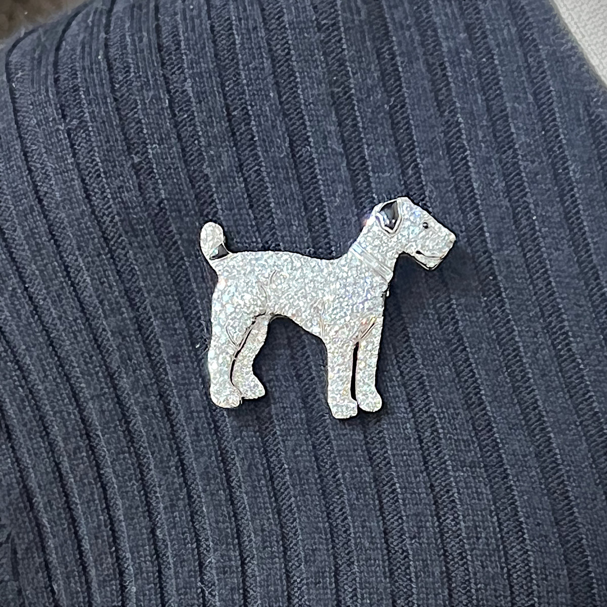 A diamond set terrier dog brooch with black onyx details, in platinum, modelled on a blue sweater
