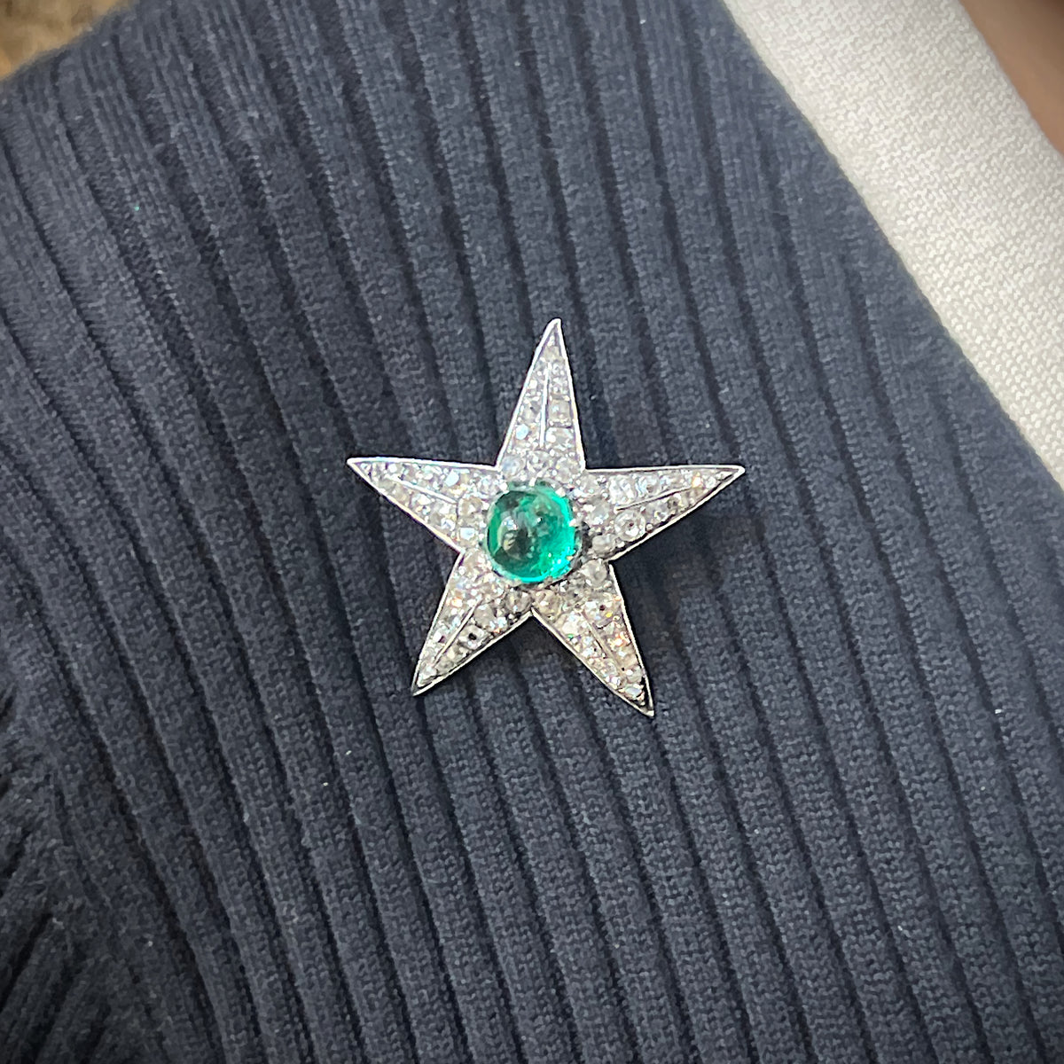 A star shaped brooch in silver and gold, with a cabochon emerald centre surrounded by old cut diamonds, modelled on a blue sweater