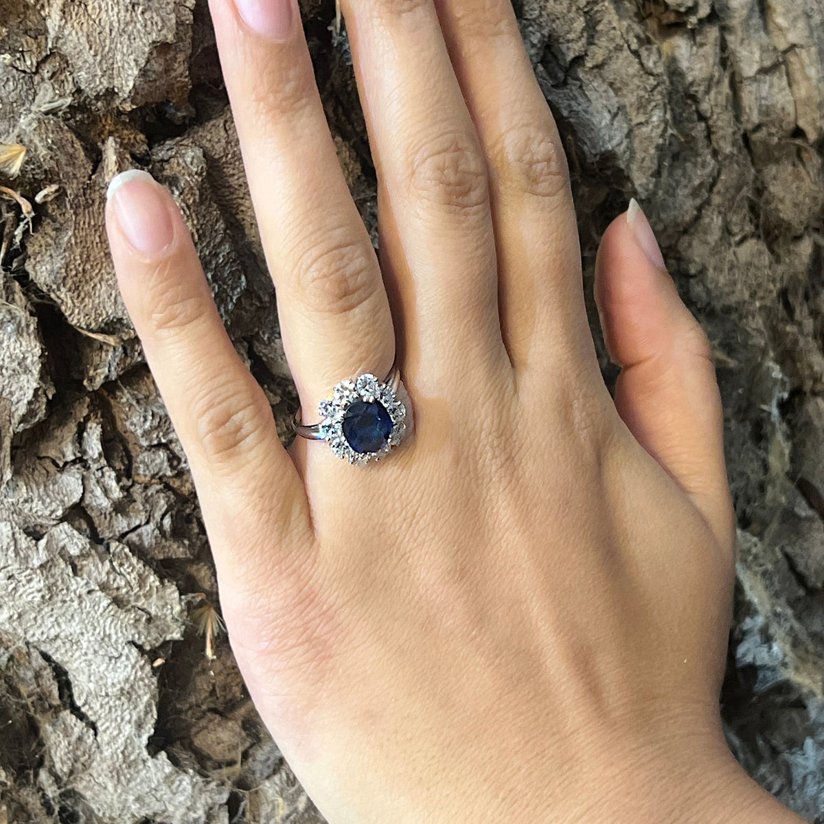 An oval sapphire and round diamond claw set cluster ring in platinum, modelled on a hand