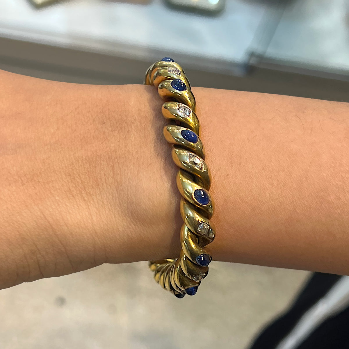 A yellow gold twisted bracelet set with cabochon sapphires and old cut diamonds, modelled on a wrist