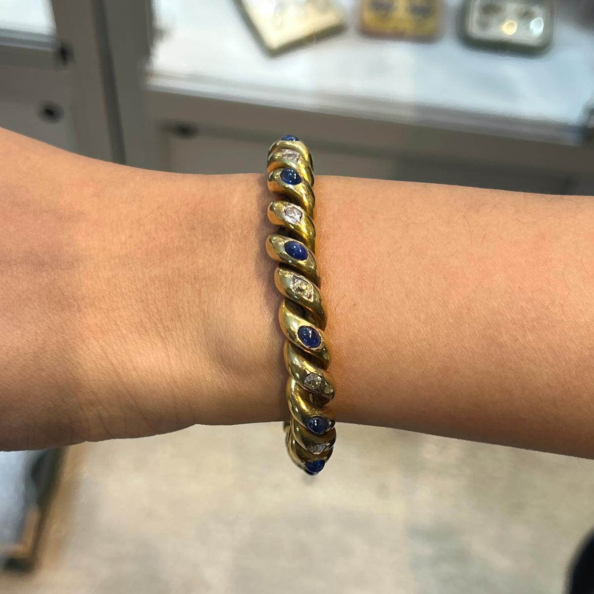 A yellow gold twisted bracelet set with cabochon sapphires and old cut diamonds, modelled on a wrist