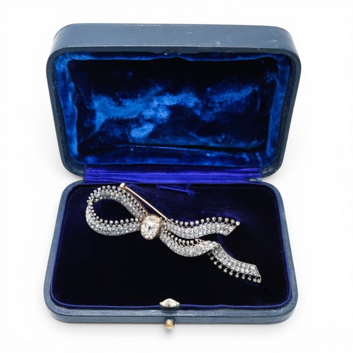 An ornate bow brooch set with diamonds, in silver and yellow gold, in a blue velvet box