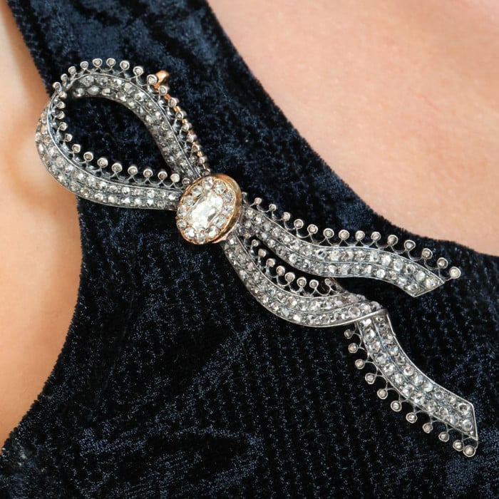 An ornate bow brooch set with diamonds, in silver and yellow gold, modelled by a woman wearing a black top