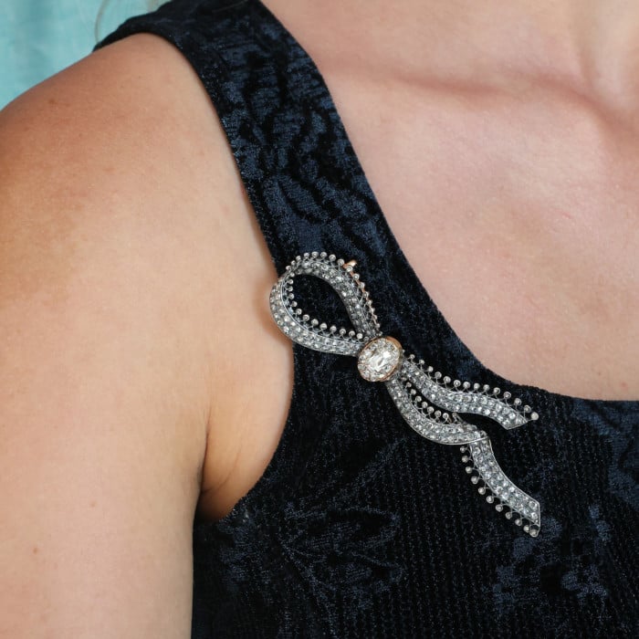 An ornate bow brooch set with diamonds, in silver and yellow gold, modelled by a woman wearing a black top