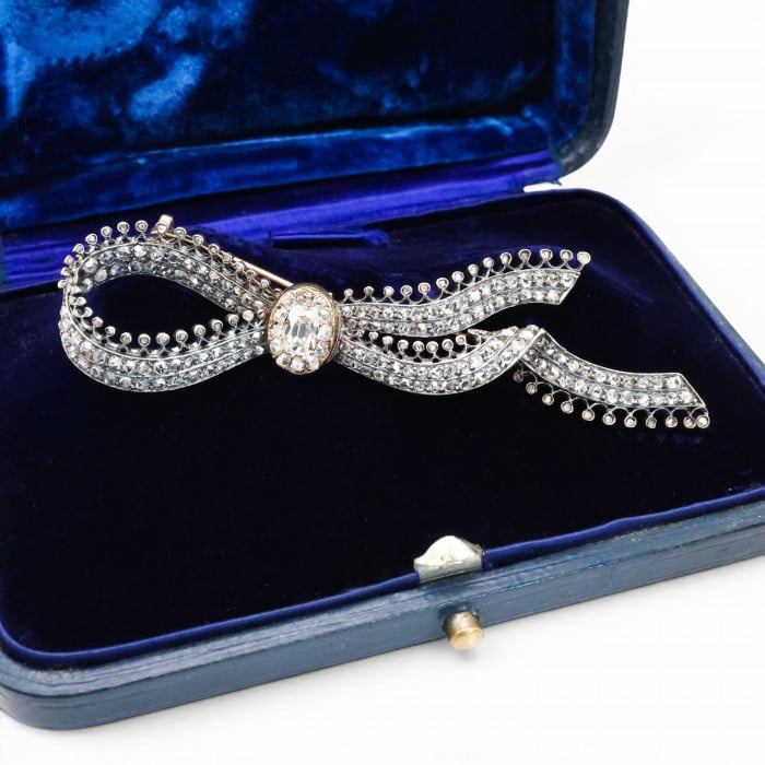 An ornate bow brooch set with diamonds, in silver and yellow gold, in a blue velvet box