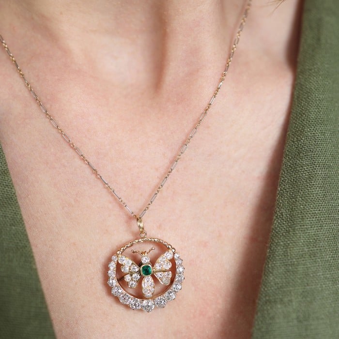 A butterfly open circle pendant set with an emerald and diamonds, in yellow gold, with a chain, modelled