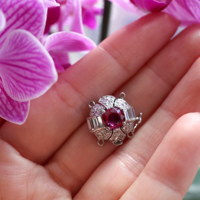 A ruby and diamond clasp in white metal, held in a hand