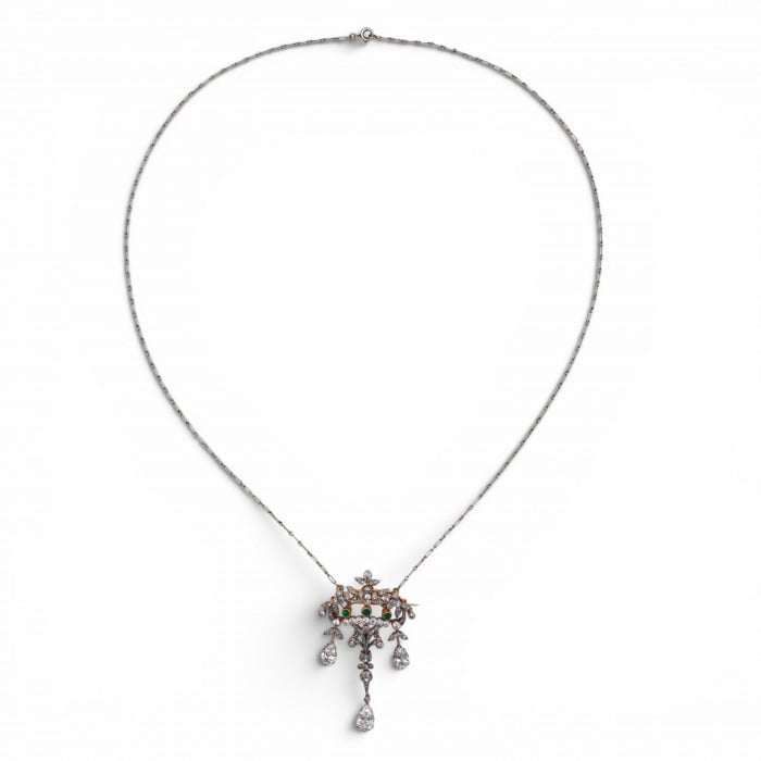 An ornate floral and leaf motif drop pendant necklace set with diamonds and emeralds, with integrated chain, in platinum and gold