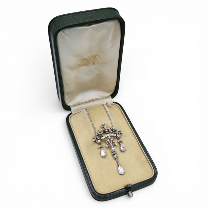 An ornate floral and leaf motif drop pendant necklace set with diamonds and emeralds, with integrated chain, in platinum and gold, in an antique fitted box