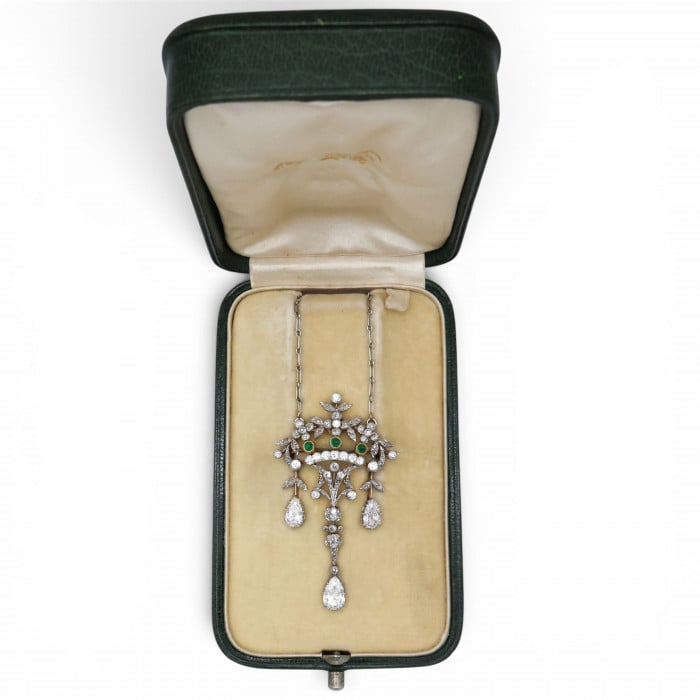 An ornate floral and leaf motif drop pendant necklace set with diamonds and emeralds, with integrated chain, in platinum and gold, in an antique fitted box