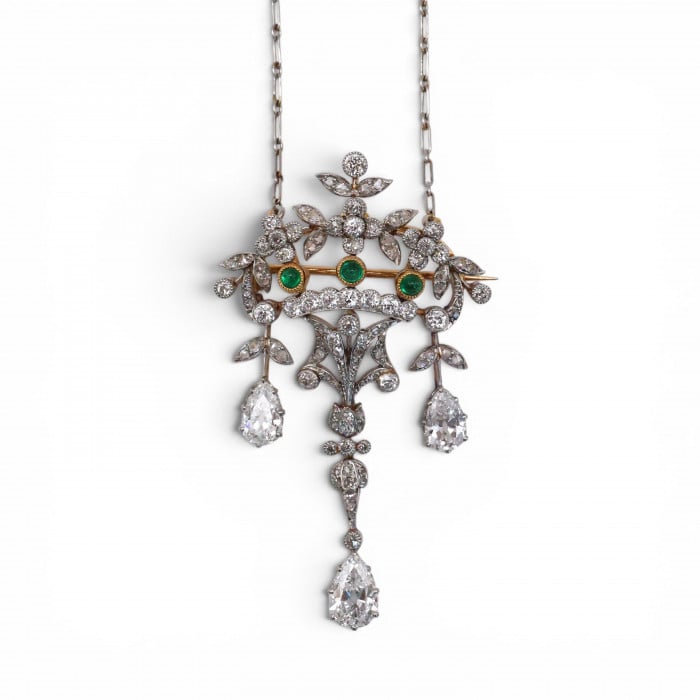 An ornate floral and leaf motif drop pendant necklace set with diamonds and emeralds, with integrated chain, in platinum and gold