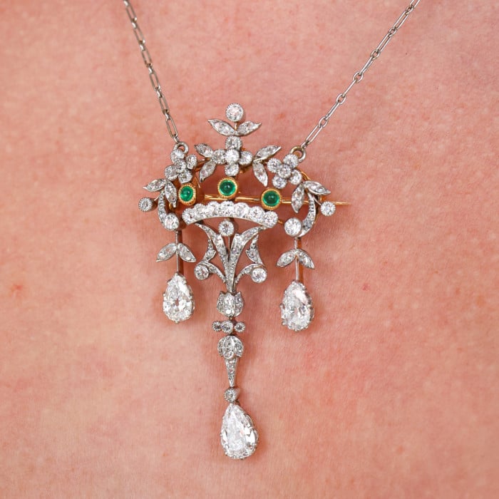 An ornate floral and leaf motif drop pendant necklace set with diamonds and emeralds, with integrated chain, in platinum and gold, modelled by a woman